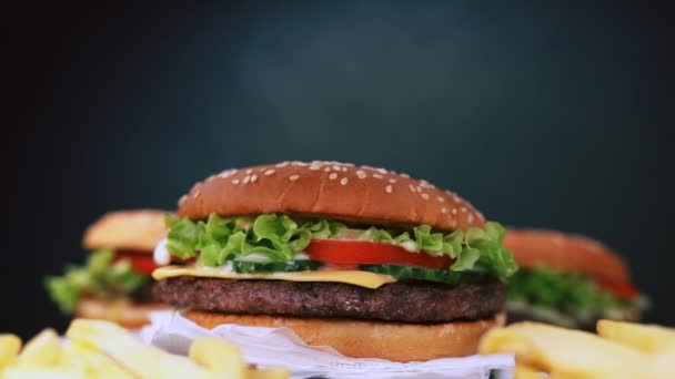 Смачна смажена яловичина гамбургери обертається на чорний дим фону з Патті, овочі, сир, салат і майонез. Американська швидкого харчування, нездоровий жиру фаст-фудом концепції — стокове відео