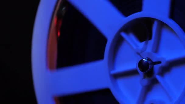 Gros plan d'une bobine. Vieux projecteur de film 8mm montrant un film la nuit dans une pièce sombre avec lumière bleue. Objets rétro vintage, concept cinématographique — Video