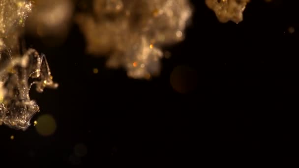 Gyllene bläck i vattenfotografering med höghastighetskamera. Gulddroppar av färg tappas, reagerar, skapar abstrakta moln formationer metamorfos på svart. Konstbakgrunder — Stockvideo