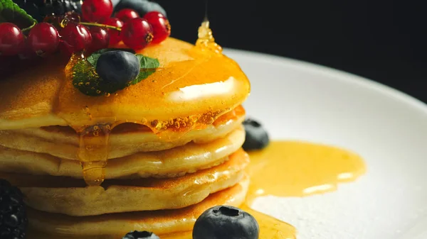 Stack of homemade pancakes or crepes decorated on top with forest berries - red currant, blackberry and blueberry. Delicious, healthy classic american breakfast. Close-up
