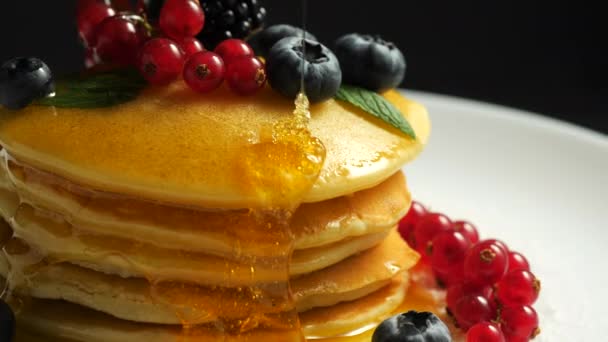 Stack of fresh fluffy pancakes decorated on top with forest berries rotating on plate and pouring honey syrup. Delicious, healthy american breakfast. Fresh bakery concept. 4k. — Stock Video