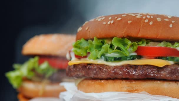 Свіжі смачні гамбургери на грилі обертаються на фоні чорного диму. М'ясні пиріжки, помідори, огірок, салат і насіння кунжуту. Концепція фаст-фуду. соковитий спосіб життя їжі . — стокове відео