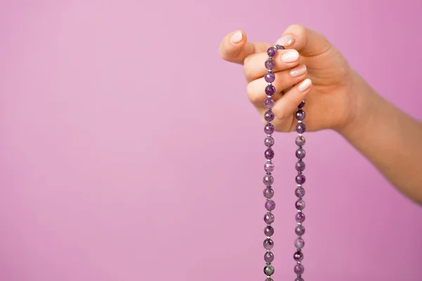 Femme, main éclairée rapprochée, compte Malas, brins de perles de pierres précieuses utilisés pour tenir compte pendant les méditations du mantra sur fond rose — Photo