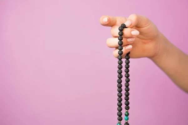Femme, main éclairée rapprochée, compte Malas, brins de perles de pierres précieuses utilisés pour tenir compte pendant les méditations du mantra sur fond rose — Photo