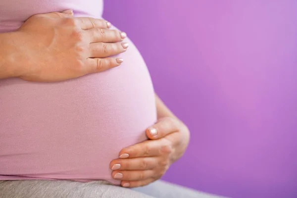 Κρατώντας τα χέρια στην κοιλιά κοιλιά εγκύου γυναίκας. Νεαρό κορίτσι περιμένοντας μωρό σε ροζ bakcground. Μητρότητας, μητρότητας, ιδέα της εγκυμοσύνης. Χώρο αντίγραφο — Φωτογραφία Αρχείου