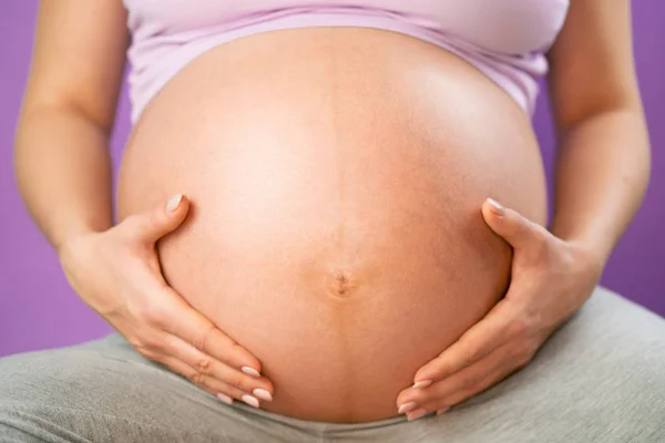 Κρατώντας τα χέρια στην κοιλιά κοιλιά εγκύου γυναίκας. Νεαρό κορίτσι περιμένοντας μωρό σε ροζ bakcground. Μητρότητας, μητρότητας, ιδέα της εγκυμοσύνης — Φωτογραφία Αρχείου