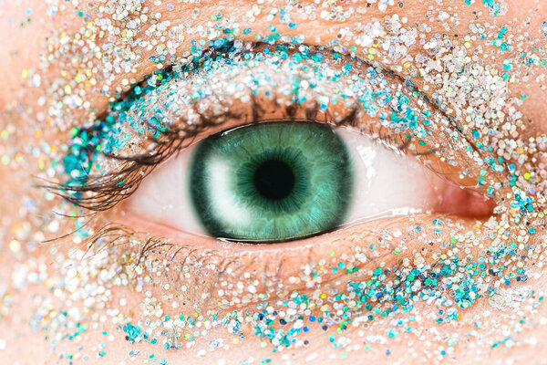 Macro green female eye with glitter eyeshadow, colorful sparks, crystals. Beauty background, fashion glamour makeup concept. Holiday evening make-up detail.