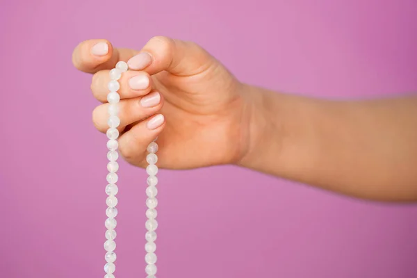 Femme, main éclairée rapprochée, compte Malas, brins de perles de pierres précieuses utilisés pour tenir compte pendant les méditations du mantra sur fond rose — Photo