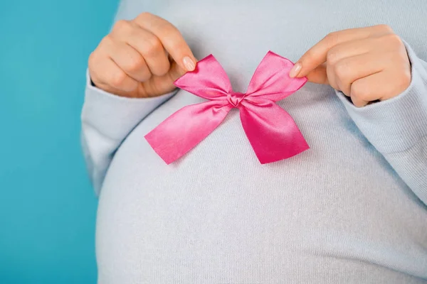Έγκυος γυναίκα κρατώντας ροζ φιόγκο σε κοιλιά κοιλιά φόντο. Νεαρό κορίτσι περιμένοντας μωρό. Μητρότητας, μητρότητας, εγκυμοσύνη, έννοια αγάπης — Φωτογραφία Αρχείου