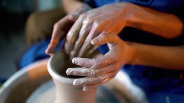 Hands of potter and his female student. Man and woman working together, creating clay product on potter wheel. Traditional pottery making, teacher shows basics of pottery in art studio — Stock Video