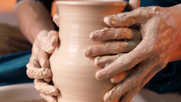 Manos de alfarero y su alumna. Hombre y mujer trabajando juntos, creando producto de arcilla en la rueda de alfarero. Fabricación de cerámica tradicional, profesor muestra los fundamentos de la cerámica en el estudio de arte — Vídeos de Stock