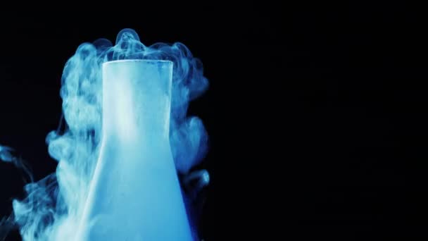 Cold blue flask with liquid nitrogen on black background. Concept of chemical experiments and tests. Edutainment. Copy space. 4k. — Stock Video