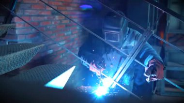 Metal kaynak. Koruyucu maske demir merdiven üzerinde çalışan erkek kaynakçı. Endüstriyel yapı kavramı. Modern kaynak makinesinden kıvılcım. Ağır çekim