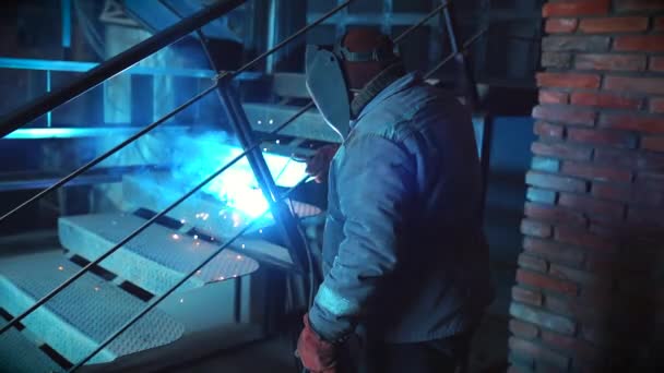 L'uomo irriconoscibile in indumenti protettivi e maschera in fabbrica di costruzione è impegnato in lavori di saldatura. Concetto di costruzione e lavoro con il metallo. Scintille da macchina moderna . — Video Stock