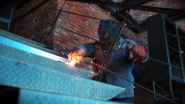 Oigenkännlig mannen i skyddskläder och mask konstruktion fabriken bedriver svetsarbeten. Begreppet byggnad och arbete med metall. Gnistor från modern maskin. — Stockvideo