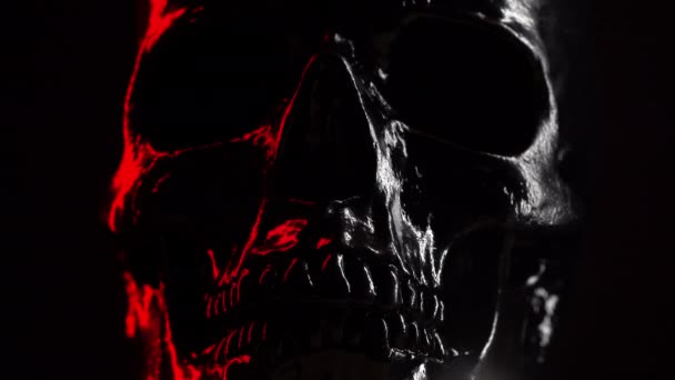 Model of human skull painted with black on dark background with variable red illumination. Spooky and sinister., Halloween celebration — Stock Video