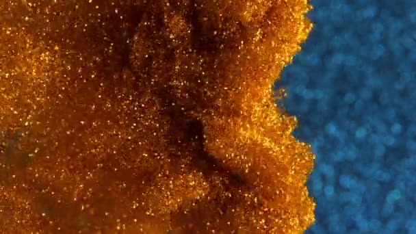 Tinta mágica en el agua. Partículas doradas brillantes con pintura brillante creando formaciones abstractas de nubes. Universo polvo de oro sobre fondo bokeh azul — Vídeo de stock