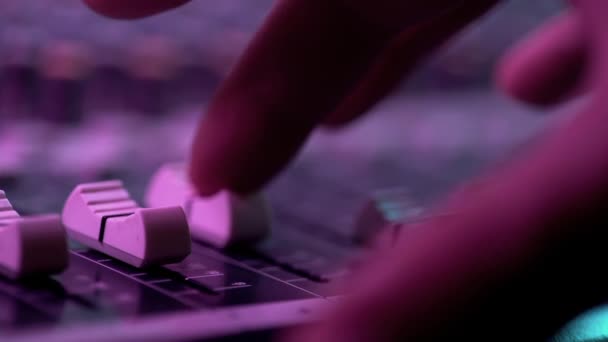 Mão de engenheiro de som trabalhando com fader no console mixer no concerto de música. Vista de perto. Luz de néon colorido — Vídeo de Stock