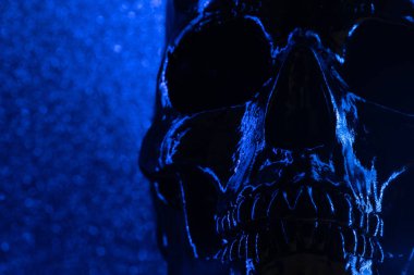 Bokeh ile karanlık arka planda insan mavi kafatası. Korku, ölüm ve korku kavramı, Cadılar Bayramı kutlamasıdır. Ürkütücü ve uğursuz.