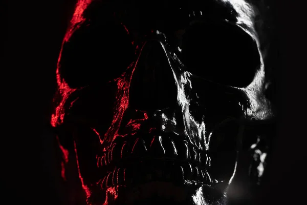 Modelo de crânio humano pintado com preto sobre fundo escuro com iluminação. Conceito de medo e horror, celebração de Halloween. Espaço de cópia — Fotografia de Stock
