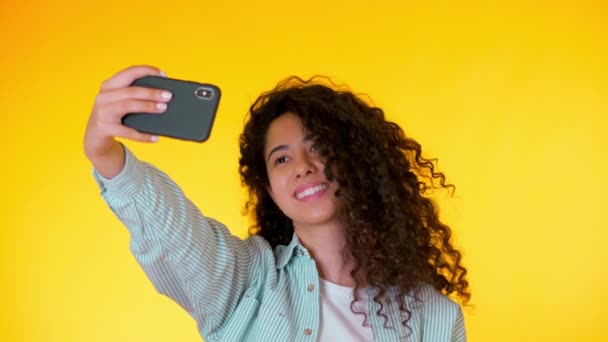 Bella donna con i capelli ricci in possesso e utilizzando lo smart phone per filmarsi in studio giallo. Donne che utilizzano la tecnologia di networking in vacanza, stile di vita. 4k . — Video Stock