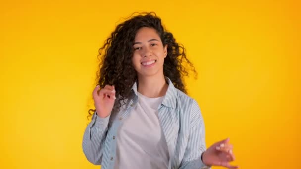 La chica se mueve al ritmo de la música. Woamn con pelo rizado bailando sobre fondo amarillo. Mujer divirtiéndose. Ella sonriendo, el pelo ondeando maravillosamente. Increíbles imágenes positivas . — Vídeo de stock