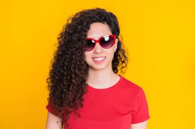 Sarı arka planda kıvırcık saç stili ile güzel kız. Kırmızı t-shirt gülümseyen ve kamera bakıyor kadın güzel portre. Latin veya İspanyol yarışı genç model