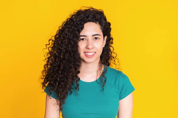 Pretty girl with curly hairstyle on yellow background. Beautiful portrait of woman in green t-shirt smiling and looking at camera. Latin or hispanic race young model. — Stock Photo, Image