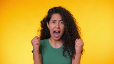 Yeşil t-shirt bir şey korkuyor kıvırcık saçlı korkmuş İspanyol kadın ve sarı arka plan üzerinde korku dolu büyük gözleri ile kamera içine bakıyor