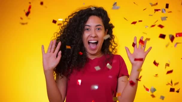 Młoda dziewczyna Łacińskiej z kręcone włosy taniec i zabawy w konfetti deszcz na żółtym tle. Kobieta celebruje, przedstawia radość i szczęście. Sukces, zwycięstwo, koncepcja święta. — Wideo stockowe