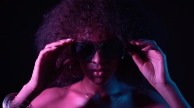 Kıvırcık afro saç ile çekici alışılmadık kız gözlüklerini düzeltir. Mükemmel makyaj kamera bakıyor ve gülümseyen seksi kadın. Glamour, moda konsepti
