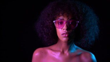 Makyaj ve şeffaf gözlük gece karanlık odada poz ile baştan çıkarıcı kadın. Neon ışık genç çekici karışık yarış kız portresi. Moda, glamour, model konsepti