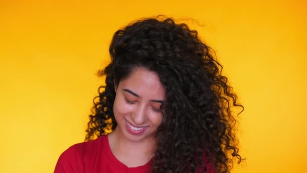 Retrato de menina latina jovem com cachos flerta no fundo amarelo. Mulher tentadora a sorrir para a câmara. Imagens do estúdio. Feminino em t-shirt vermelha, estilo casual . — Vídeo de Stock