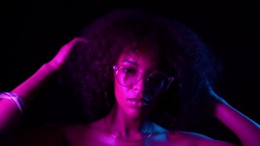 Siyah arka planda flört makyaj ve şeffaf gözlük ile seksi kadın. Neon ışıkta genç büyüleyici Afrikalı kızın portresi. Parti, gece kulübü konsepti