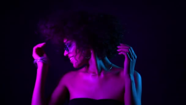 Hermosa mujer negra con cabello afro divirtiéndose sonriendo y bailando en estudio sobre fondo negro en luz de neón. cámara lenta . — Vídeos de Stock