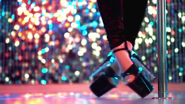 Молодая сексуальная стриптизерша, двигающаяся в туфлях на высоких каблуках со стразами на сцене с пилоном в стрип-клубе, танцы на шесте. Сияющий фон. Танец, секс, искушение — стоковое видео