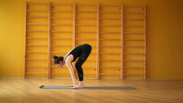 Surya Namaskar. Mujer en traje negro haciendo práctica de yoga en estudio amarillo sobre fondo de escaleras. Salud, estilo de vida, concepto deportivo — Vídeos de Stock