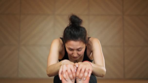 Mulher bonita nova que pratica no ioga na sala de aula minimalista clara do estúdio. Menina dentro de casa no espaço de retiro fazendo postura de curvatura para a frente sentada - Paschimottanasana — Vídeo de Stock