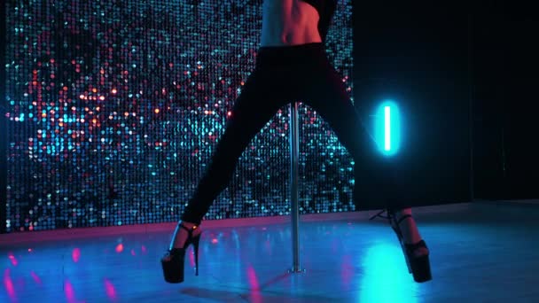 Poledance op glanzende muur achtergrond. Benen in hakken schoenen van onherkenbaar vrouw doen trucs met pylone. Jong meisje met lang haar in zwart dansen seksueel met Pole in Studio. — Stockvideo