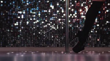 Genç striptizci gece kulübünde yüksek topuklu ayakkabılarla dans eder ve ziyaretçileri baştan çıkarır. Parlak duvarda dans eden kadın