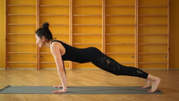 Meisje binnenshuis in retraite ruimte doen hand stand pose. Sterke handen. Jonge vrouw in het zwart beoefenen van yoga in lichte minimalistische studio klasse kamer. Health lifestyle concept. — Stockvideo