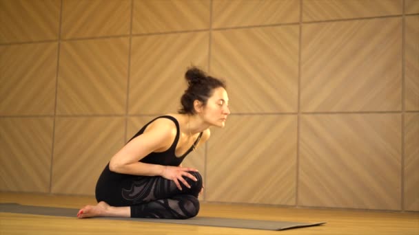Young pretty woman practicing yoga at light minimalist studio class room. Girl doing stretching in sitting position. Health lifestyle concept. — 비디오