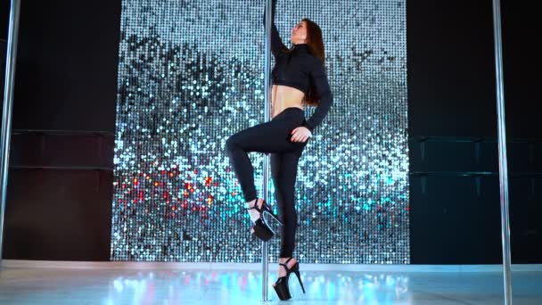 Σέξι χορεύτρια σε μαύρο κινούμενο με ψηλά τακούνια παπούτσια με pylone στο νυχτερινό κέντρο ή στούντιο. Χορεύοντας με τους πόλους. Λαμπερό φόντο. Χορός, σεξ, έννοια πειρασμός. — Αρχείο Βίντεο