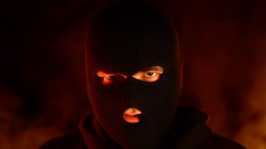 Yanan bir gece yangınının arka planında siyah balaclava genç adamın portresi. Kitlesel mitingler ve ayaklanmalar kavramı