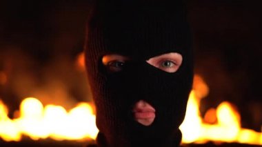 Yanan gece yangınının arka planında siyah maskeli genç kadın ultras veya protestocu portresi. Kitlesel mitingler ve ayaklanmalar kavramı