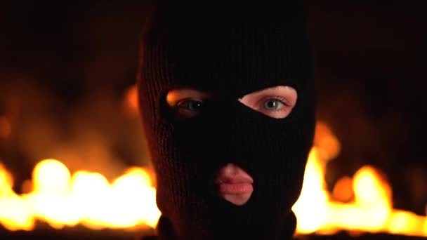 Портрет молодой женщины ультрас или протестующей в черной маске на фоне пылающего ночного огня. Концепция массовых митингов и беспорядков — стоковое видео