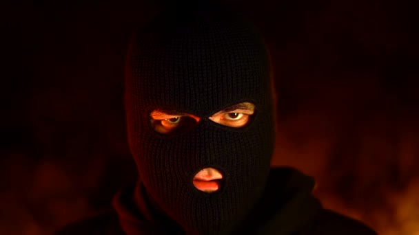 燃える火の背景に対するストリートの戦いの間に黒いマスクを着けた若者の肖像画。政治的ストライキとフーリガンの概念 - ウルトラ. — ストック動画