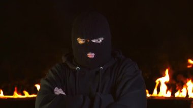 Balaclava'daki adamın portresi yanan ateşe karşı baş pozitif jest gösteriyor