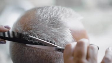 Kadın kuaför, gri saçlı adamı kesmek için makas kullanıyor. Berber bir adamın saçını kesmek için makas kullanıyor. Yakın çekim, yavaş çekim..