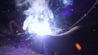 Fabrikada işçilerin öğütülmesi ve kaynaklanması. Endüstriyel bir fabrikada kaynak. Ağır çekim. Parlamalar ve karanlıkta inşaat alanında kaynakçılık yaparken çıkan kıvılcımlar.